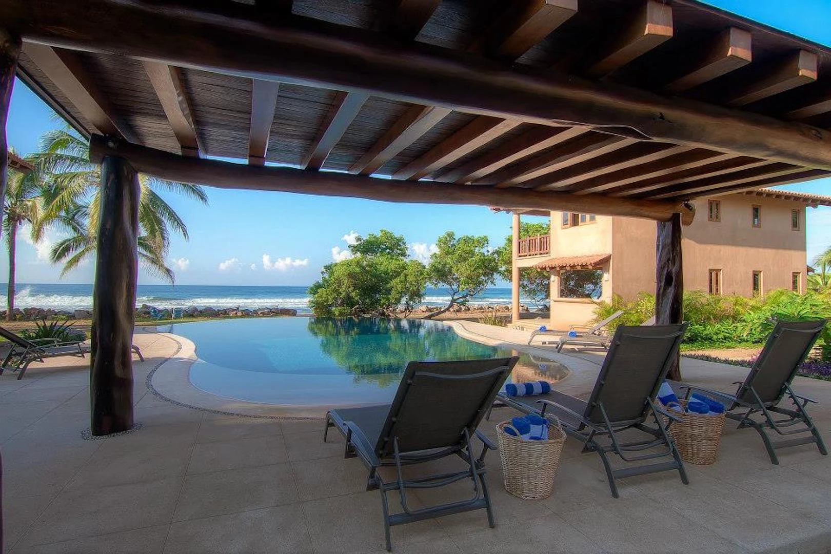Shaded poolside terrace overlooking the infinity pool and Pacific Ocean